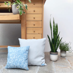 Blue leather Gerbera pillow styled with blue fabric pillow and flower pots with plants.