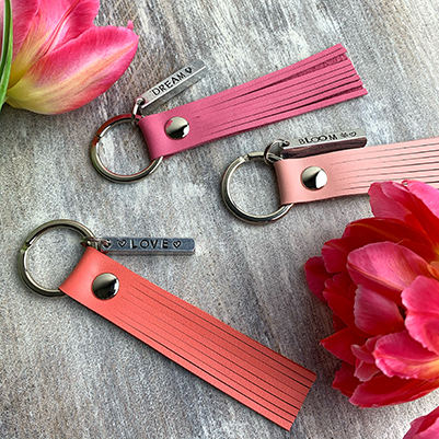 Flatlay van 3 lederen flosh sleutelhangers in de kleuren nude pink, hot pink en coral kleur, en 2 roze tulpen.